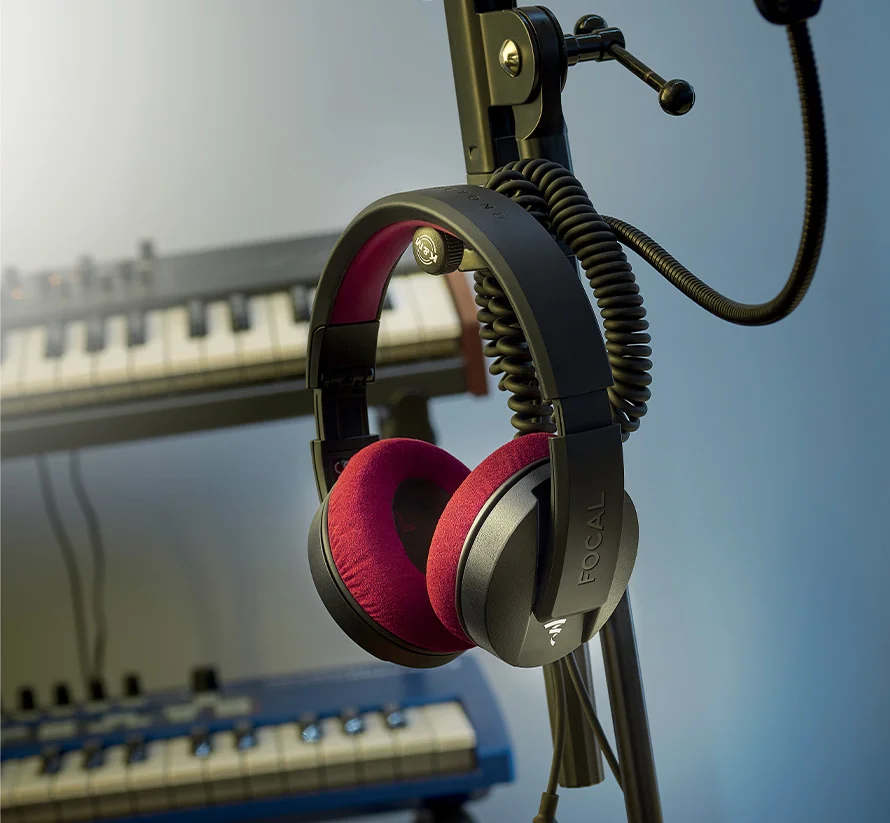 Auriculares profesionales Focal Listen Pro colgados sobre un soporte en un estudio con varios teclados al fondo.