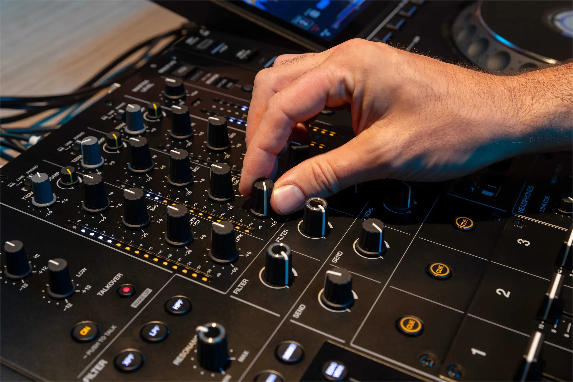 DJ utilizando la mesa de mezclas AlphaTheta DJM-V5 en sesión real, ajustando controles de ecualización y efectos durante una mezcla profesional.